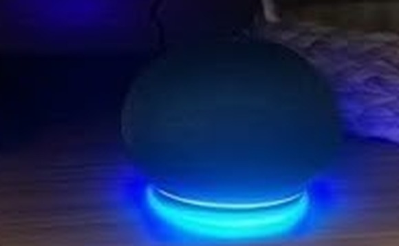 Smart speaker Alexa Echo com anel de luz azul aceso sobre um móvel